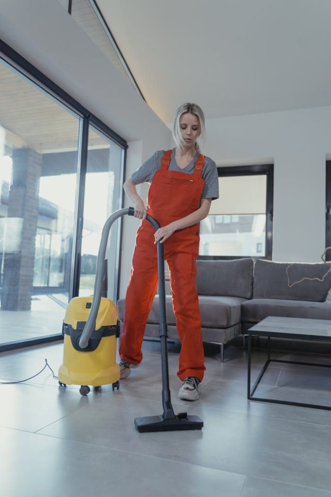A woman in red overalls vacuuming a modern living room for cleanliness and hygiene.
