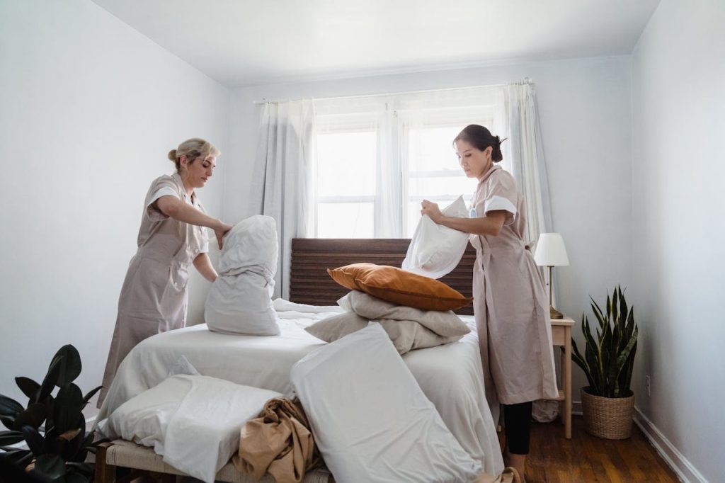 Two women in uniforms tidying a bed, creating a clean and welcoming space.